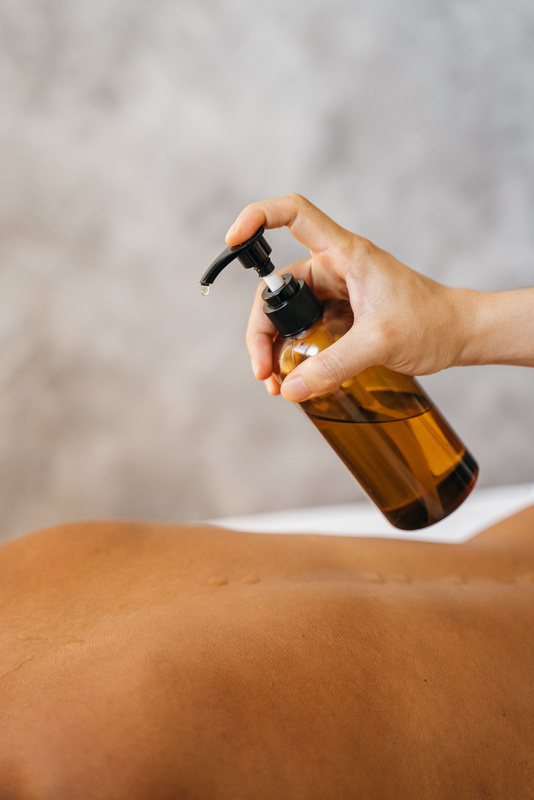 A Massage Therapist Putting Oil on a Client's Bare Back